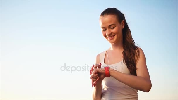 Joven mujer bastante sonriente utilizando su dispositivo smartwatch fuera . — Vídeo de stock