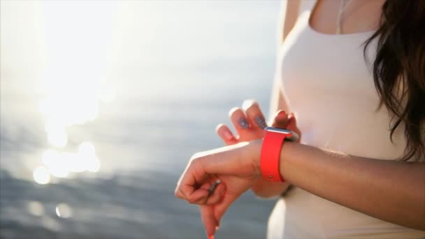 Feche as mãos da mulher tiro usando relógios inteligentes na frente do mar durante o pôr do sol . — Vídeo de Stock
