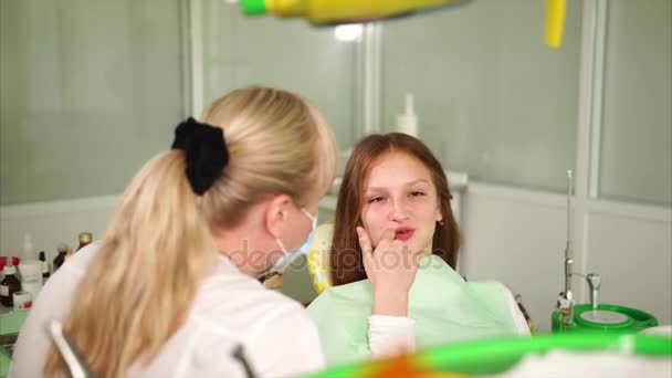 Der Arzt der Klinik erklärt dem Teenager die Behandlung der Mundhöhle — Stockvideo