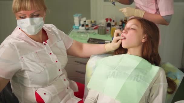 女孩在牙科内阁坐在扶手椅上。牙医工作与她的牙齿 — 图库视频影像