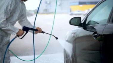 Genç beyaz adam dikkatle arabasını yıkar. Araba yıkama Self-Servis.