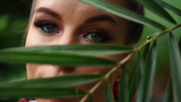 Лицо красивой молодой женщины за пальмовым листом . — стоковое видео