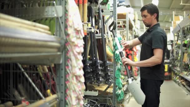 Чоловік в магазині обладнання вибирає лопату . — стокове відео