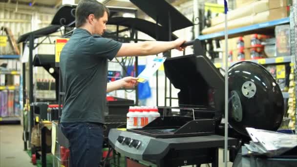 Молодий чоловік-клієнт шукає газовий гриль для барбекю в своєму заміському будинку — стокове відео