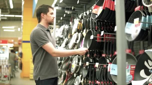 Um homem na loja a escolher utensílio. Ele tomando panela de cozinha nas mãos — Vídeo de Stock