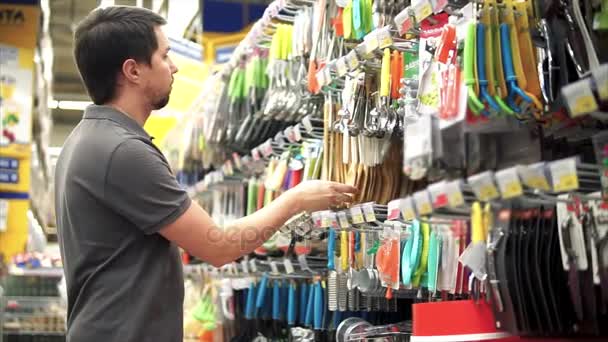 Man in de winkel in de buurt van gebruiksvoorwerp teller. Hij zoekt spatel voor zijn vrouw. — Stockvideo