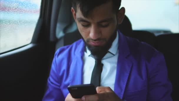 Un primo piano di un moderno uomo d'affari musulmano in macchina. Sta usando lo smartphone. — Video Stock