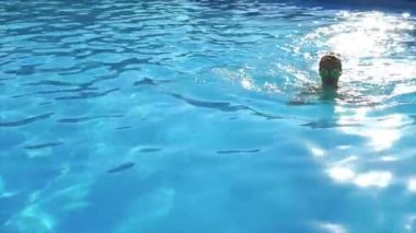 Güneş gözlüğü ve bir mayo içinde yetişkin bir kız havuzda bir yaz gününde yüzüyor.