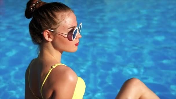 A profile of a young woman who sits by the pool and sunbaths in a swimsuit — Stock Video