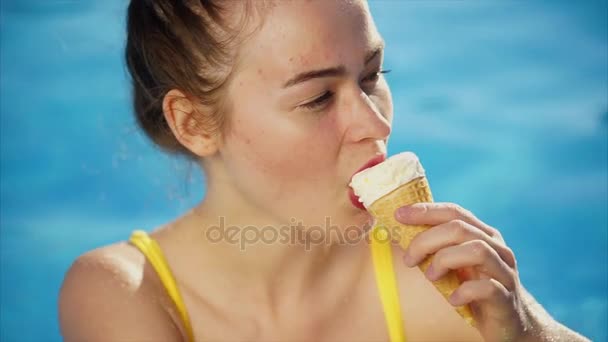 Una mujer joven y delgada, comiendo helado en un cuerno, descansa en la piscina — Vídeos de Stock