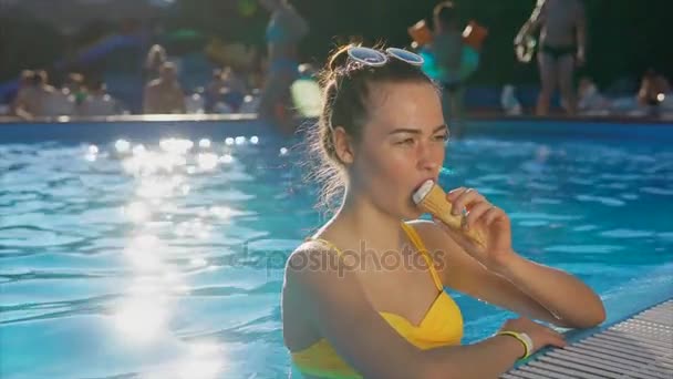 Una mujer linda y joven con un buen humor disfruta de un helado en la piscina — Vídeo de stock