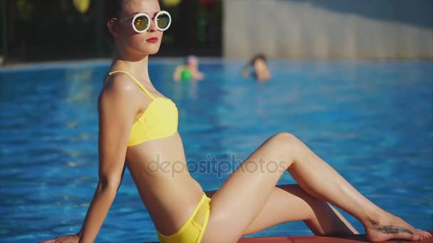 Ragazza con una buona figura prendere il sole al sole vicino alla piscina, caldo clima estivo — Video Stock