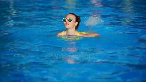 Fille élégante en lunettes de soleil nage dans la piscine sous le ciel ouvert, saison estivale — Video