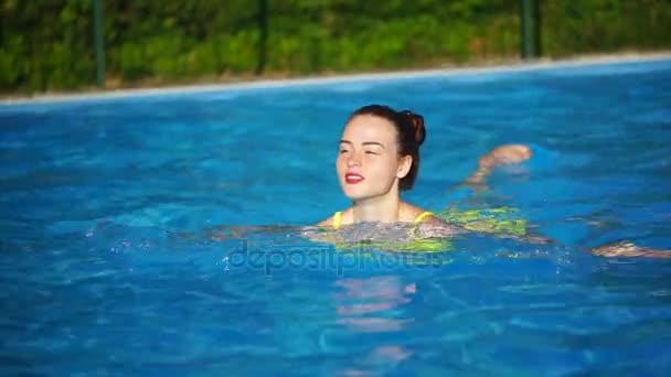 Молодая красавица плавает в бассейне и улыбается. Красивая женщина — стоковое видео