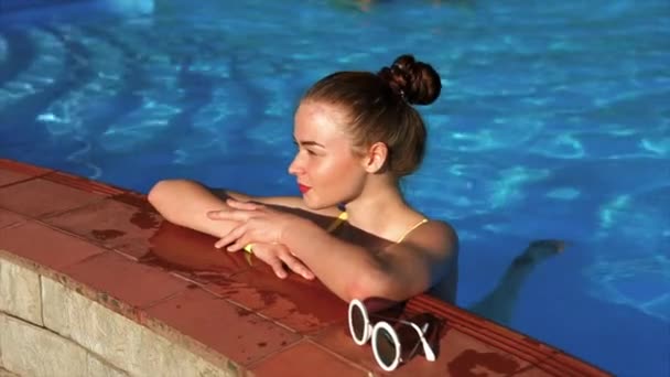 Una bonita mujer en traje de baño se relaja en una piscina en un caluroso día de verano — Vídeos de Stock
