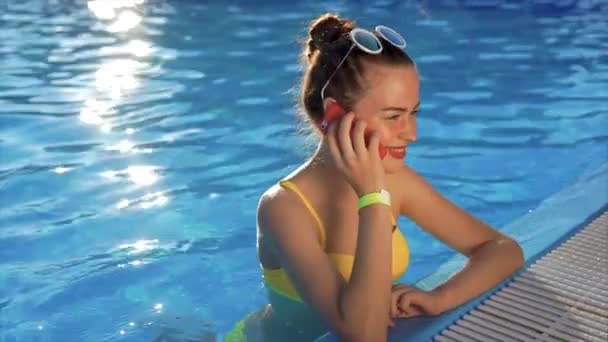 Een jonge vrouw is praten over de telefoon in het water, ze belt een vriend — Stockvideo