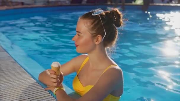 Una mujer linda y joven con un buen humor disfruta de un helado en la piscina — Vídeo de stock