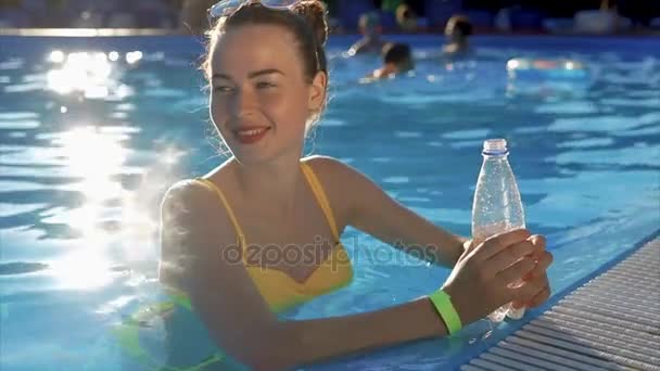 Mujer joven en traje de baño bebe agua fría de una botella de plástico en la piscina — Vídeos de Stock