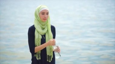 Bir hijab genç bir kadında şişe sıcak gün açık havada üzerinde maden suyu içer