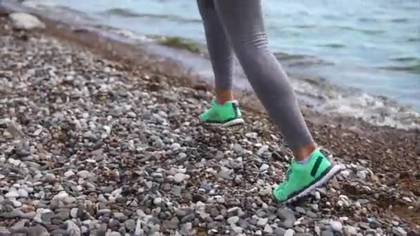 Close up shot of the feet of a young woman, she runs along the stony bank — Stock Video