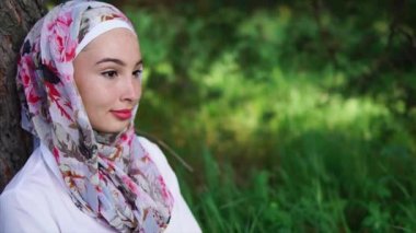 Bir ağacın yanında oturan bir düşünceli ve biraz kurnaz Müslüman kadın portresi