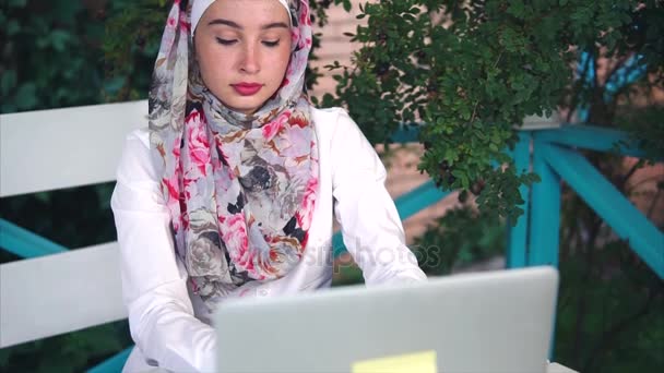 Mujer musulmana en hijab imprime mensaje en una computadora portátil, ella está afuera al aire libre — Vídeo de stock