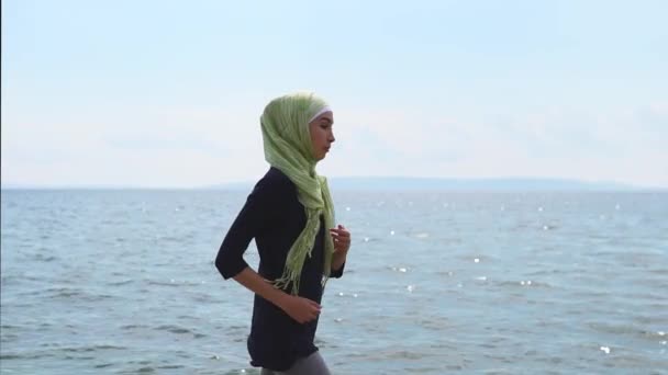 Młoda Muzułmanka idzie sportowych, w pobliżu oceanu lub morza, letni dzień — Wideo stockowe