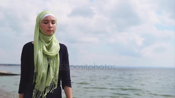 Eine junge muslimische Frau im Schleier kommt mit nachdenklichem Blick am Meer entlang — Stockvideo