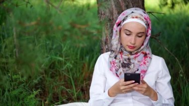 Hijab bir Müslüman telefonda arkadaşlarıyla iletişim kurmak için kullandığı bir parkta oturuyor