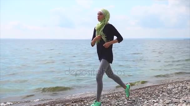 Мусульманская девушка, занимающаяся бегом на галечном пляже — стоковое видео