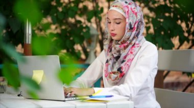 Hijab Müslüman öğrenci parkta bir dizüstü bilgisayarda bir yaz gününde bir kompozisyon yazıyor