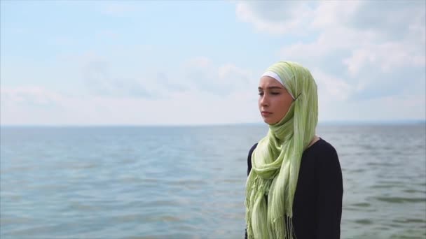 Een jonge moslimvrouw in een sluier wordt geleverd met een peinzende blik langs de zee — Stockvideo