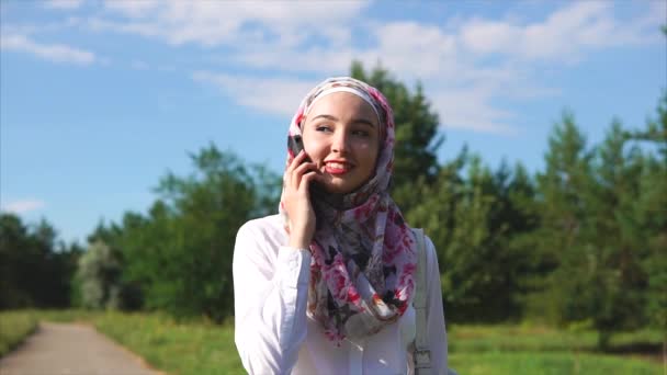 Fröhliche muslimische Frau spricht während des Spaziergangs mit Freundin auf Handy — Stockvideo
