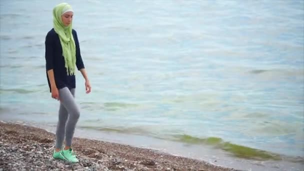 Μια νεαρή μουσουλμάνα σε ένα πέπλο έρχεται με μια σκεπτικός ματιά κατά μήκος της θάλασσας — Αρχείο Βίντεο