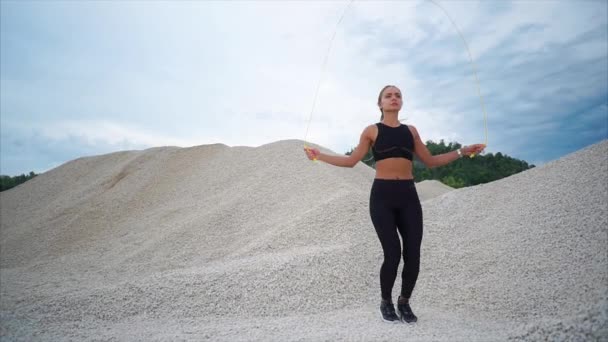 Aktívan jumping kötelet egy nyári napon egy kő háttérrel rendelkező fiatal sportoló — Stock videók