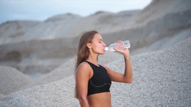 Chica tiene sed después de entrenamiento deportivo cerca de pozo de grava — Vídeo de stock