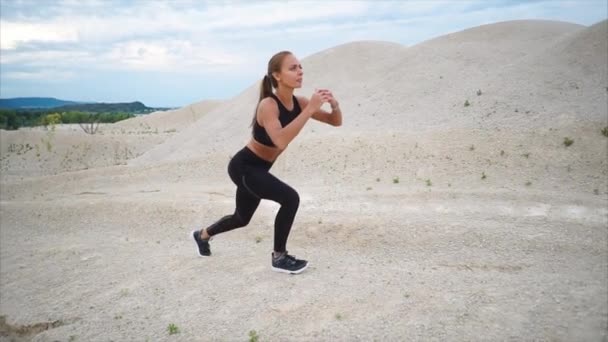 A young athlete crouches to strengthen the muscles of her legs, she is in nature — Stock Video