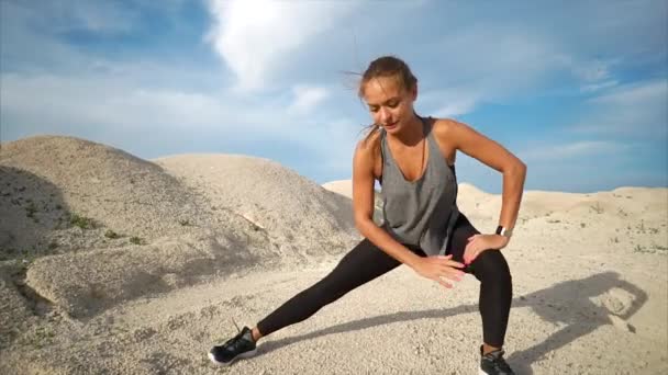 Спортсмен делает растяжения мышц ног в природе вблизи песков — стоковое видео