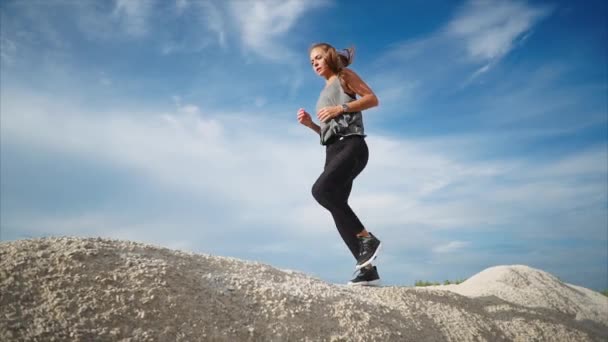 Una joven con una buena figura corre por las altas piedras de una alta montaña — Vídeo de stock