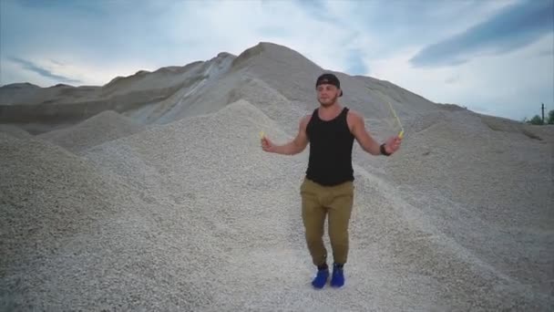 Joven saltando activamente la cuerda en la naturaleza en un día de verano con fondo de piedra — Vídeos de Stock