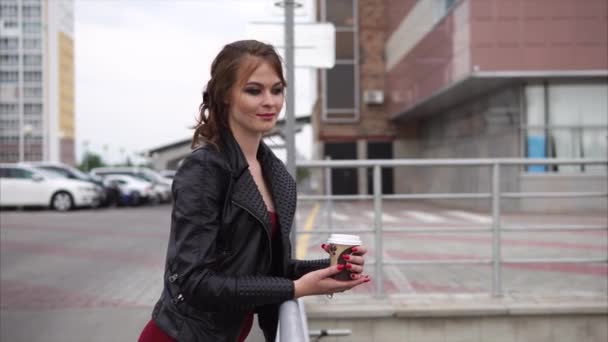 Una mujer en ropa de otoño está sosteniendo un vaso de café y mirando a la distancia — Vídeos de Stock