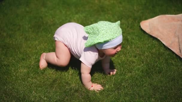 A small baby in sliders crawls along the green grass on a summer day — Stock Video