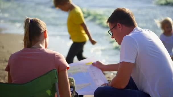 Cónyuges que tienen un mapa de papel en la mano discutir la ruta, el niño juega al lado de ellos — Vídeos de Stock