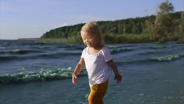 Un ragazzo corre lungo la costa vicino al lago il bambino inciampa a causa delle onde — Video Stock