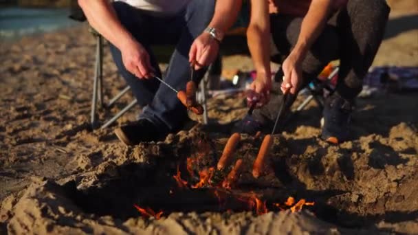 Крупным планом людей руками и телом, которые готовят мясные сосиски на костре — стоковое видео