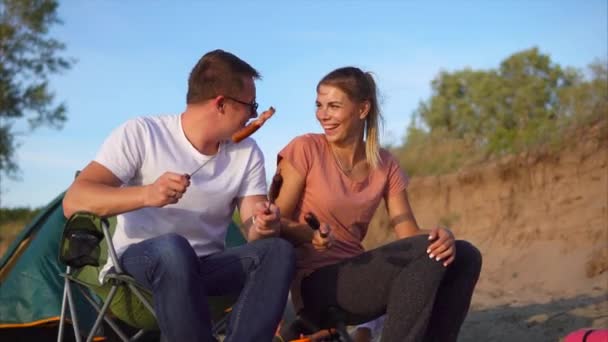 Una pareja cariñosa hablando y comiendo salchichas cocinadas en brochetas al aire libre — Vídeos de Stock