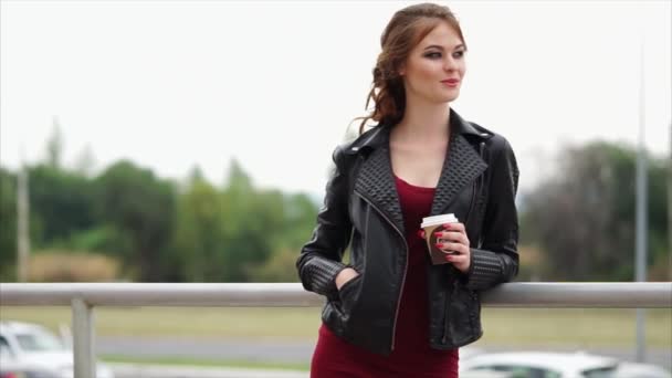 Femme romantique dans une veste en cuir et avec un café dans les mains regarde loin — Video