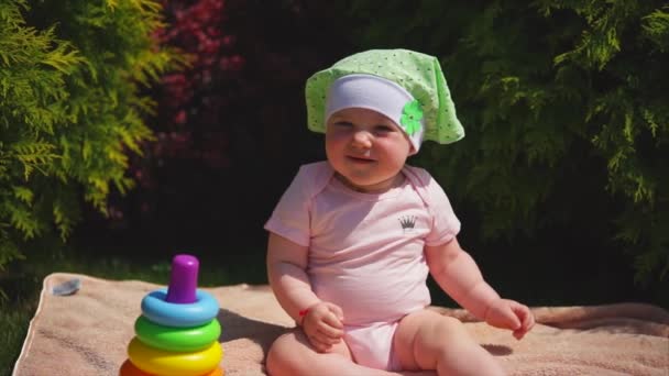 Een gelukkig pasgeboren zit op een handdoek in het park, daarna is een piramide van speelgoed — Stockvideo