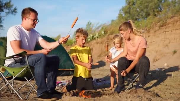 Família com crianças assando salsichas no fogo no acampamento — Vídeo de Stock