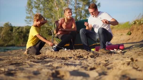 Familie roosteren marshmallow op het vuur in kamp met tent — Stockvideo